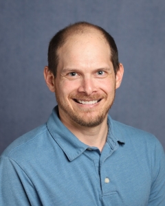 A man with short dark hair and a blue shirt