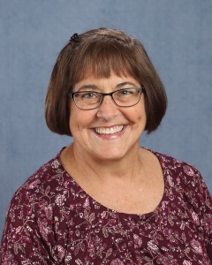 A woman with short brown hair, glasses, and patterned shirt