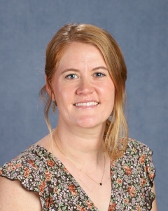 A woman with red hair tied back and patterned tank top