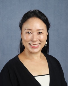 A woman with long dark hair half tied back wearing a black sweater