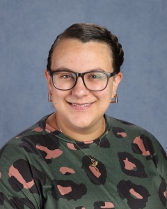 A woman with dark hair pulled tightly back with glasses and a patterned green shirt