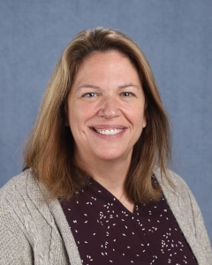 A woman with shoulder length blonde hair and a gray cardigan