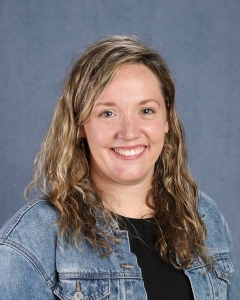 A woman with wavy brown hair and blue jean jacket