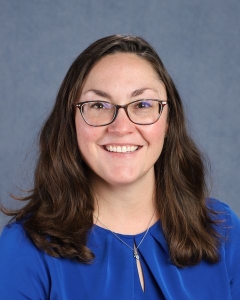 A woman with shoulder length brown hair, glasses, and a blue shirt